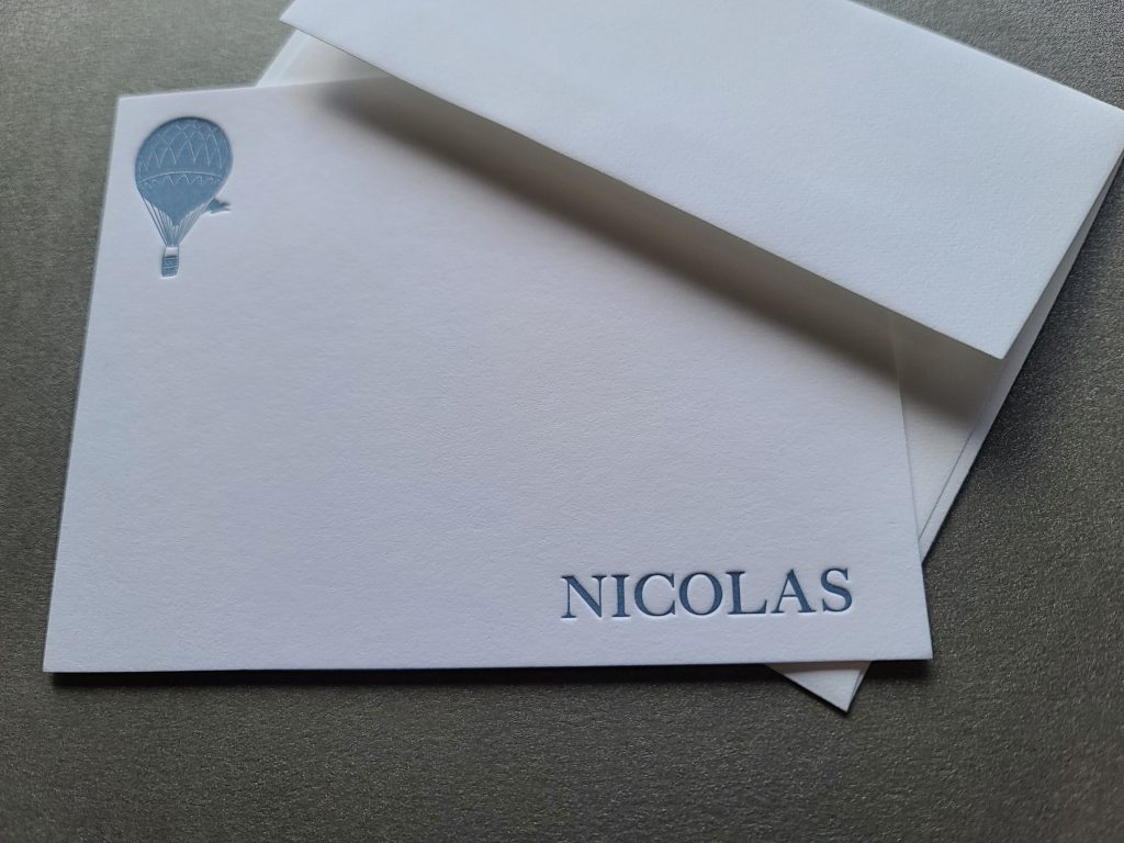 Photo shows custom stationery, with the recipient's name, Nicolas, in blue with a hot air balloon in the upper right corner.